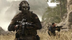 A soldier in a skull mask and sunglasses stands in the foreground while a blurry man kneels with his weapon aimed in the background