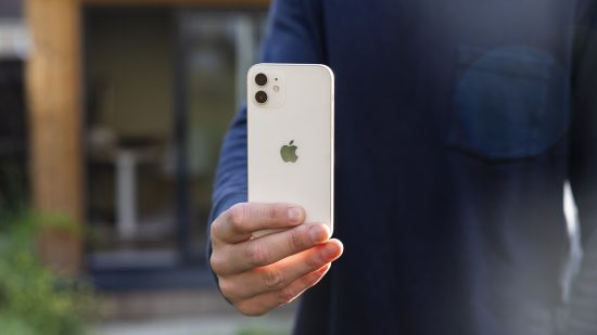 Um iPhone 12 branco nas mãos de um homem do lado de fora