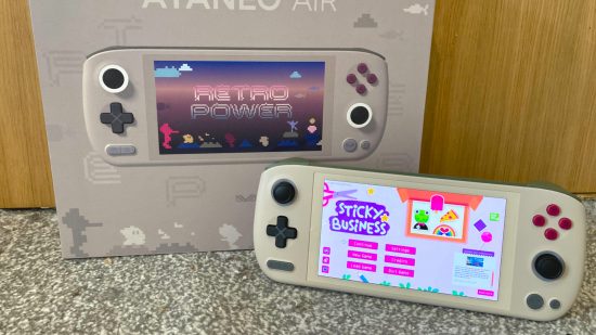 Análise do Ayaneo Air 1S: O Ayaneo exibindo Sticky Business ao lado da caixa em que veio, que também mostra o design Retro Power, em um tapete cinza e fundo de porta de madeira