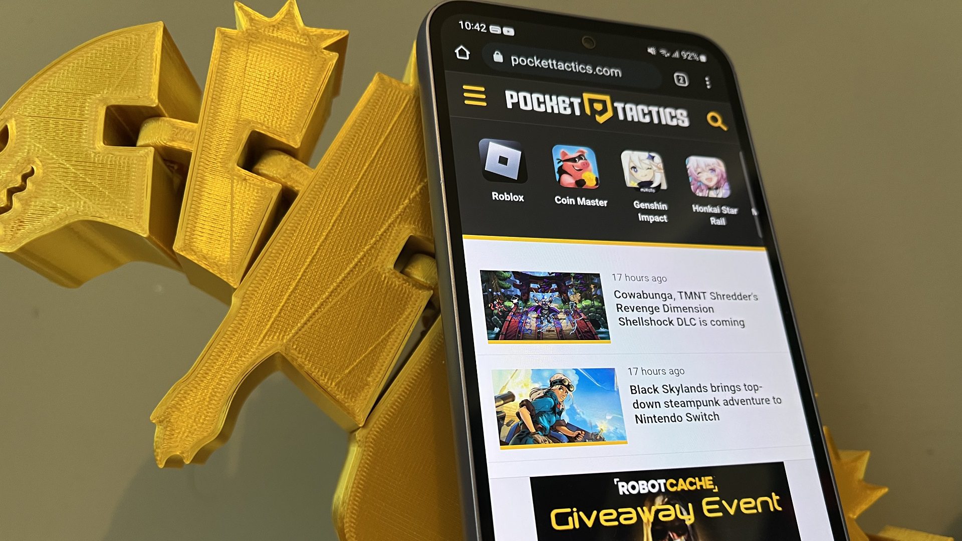 avaliação samsung a54 0 Revisão do Samsung A54 - o telefone ao lado de um dinossauro impresso em 3D com a página da Web Pocket Tactics na tela