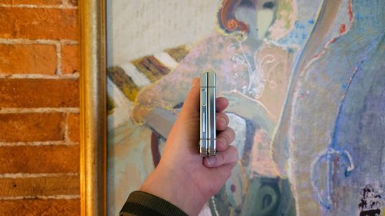 Cabeçalho do Samsung Galaxy Z Flip5 mostrando o telefone dobrado ao meio com uma mão segurando-o a partir de uma pintura abstrata de uma mulher.