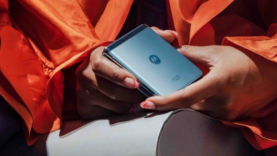 Cabeçalho da entrevista da Motorola Sudhir Chadaga mostrando um telefone preto dobrado nas mãos de alguém vestindo uma jaqueta laranja.