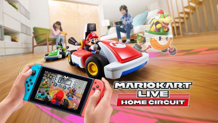 jogos de carros-mario-kart-live-home-circuit Uma pessoa segura um switch, mostrando a visão de uma câmera de um Mario Kart da vida real, que está em uma casa, com crianças brincando atrás dele, de um dos muitos jogos de carros Mario Kart Live Home Circuit.